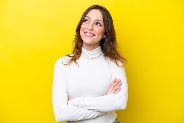 Young caucasian woman isolated on yellow background looking up while smiling