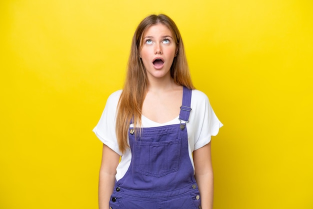 Young caucasian woman isolated on yellow background looking up and with surprised expression