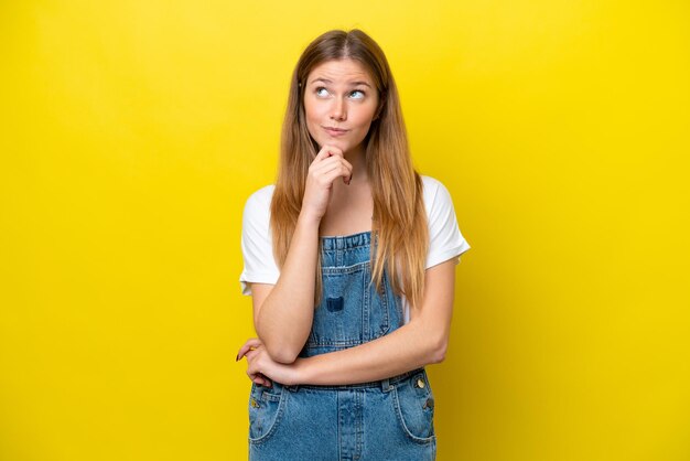 Young caucasian woman isolated on yellow background and looking up