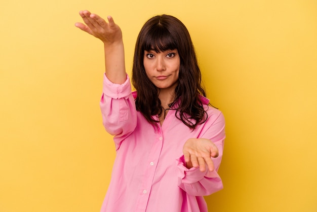 Young caucasian woman isolated on yellow background makes scale with arms, feels happy and confident.