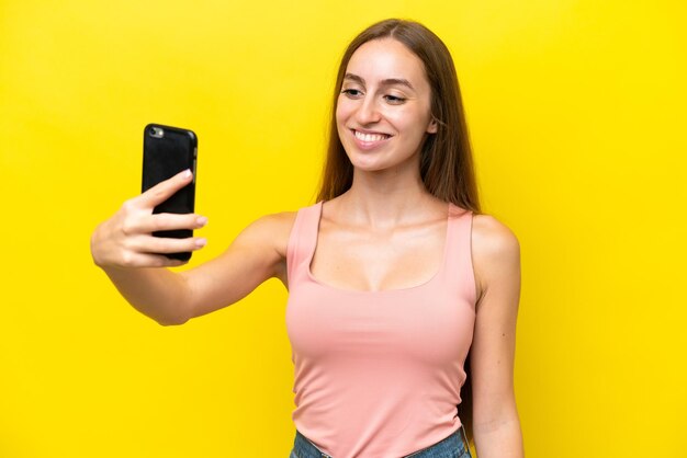 携帯電話でselfieを作る黄色の背景に分離された若い白人女性