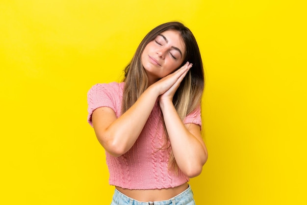 Молодая белая женщина, изолированная на желтом фоне, делает жест сна с дорабельным выражением лица.