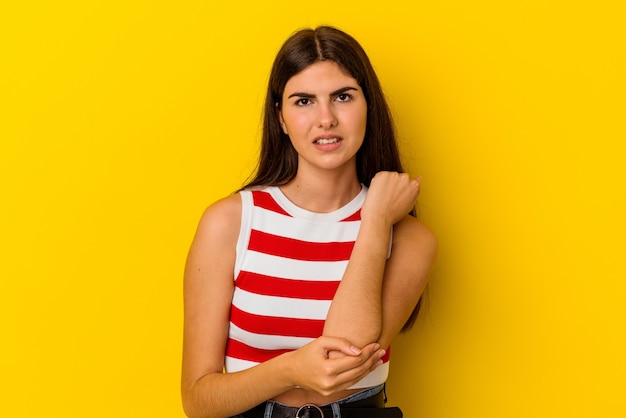 Young caucasian woman isolated on yellow background massaging elbow, suffering after a bad movement.