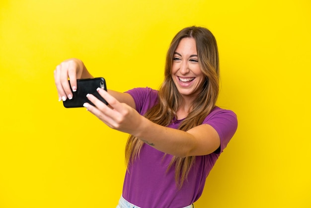 Young caucasian woman isolated on yellow background playing with the mobile phone