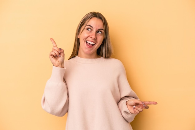 Foto giovane donna caucasica isolata su sfondo giallo che punta a diversi spazi di copia, scegliendone uno, mostrando con il dito.