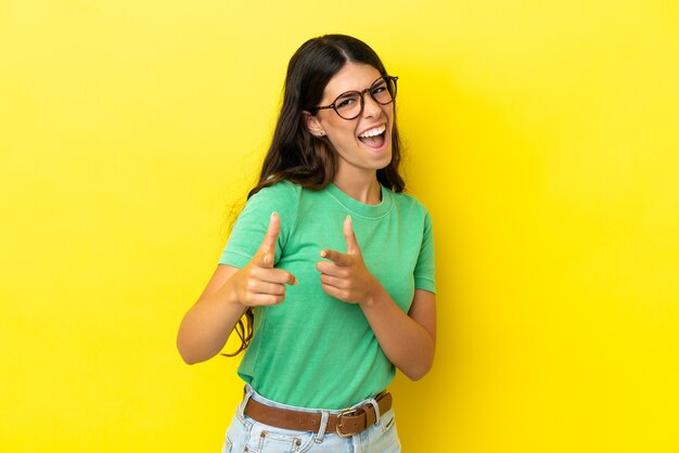 Young caucasian woman isolated on yellow background pointing to the front and smiling