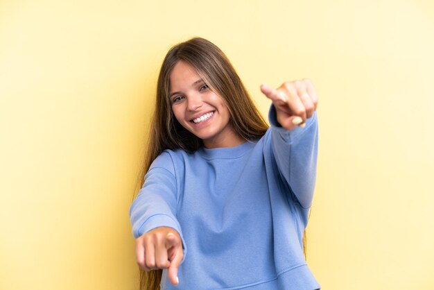 Young caucasian woman isolated on yellow background pointing front with happy expression