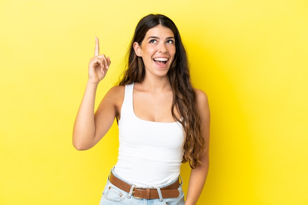 Young caucasian woman isolated on yellow background pointing up and surprised