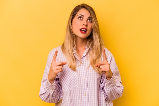 Young caucasian woman isolated on yellow background pointing upside with opened mouth