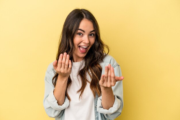 Young caucasian woman isolated on yellow background pointing with finger at you as if inviting come closer