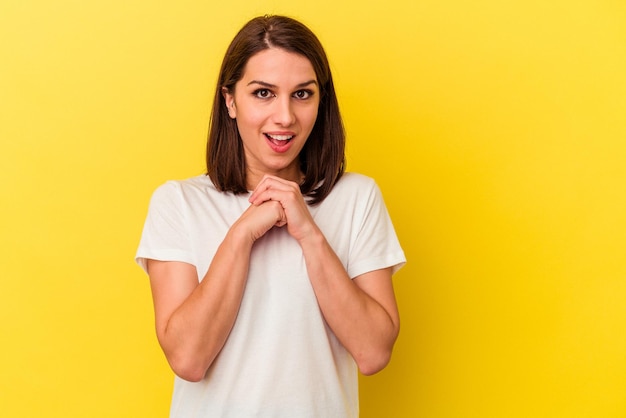 Young caucasian woman isolated on yellow background praying for luck amazed and opening mouth looking to front