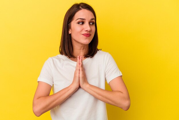 Young caucasian woman isolated on yellow background praying showing devotion religious person looking for divine inspiration