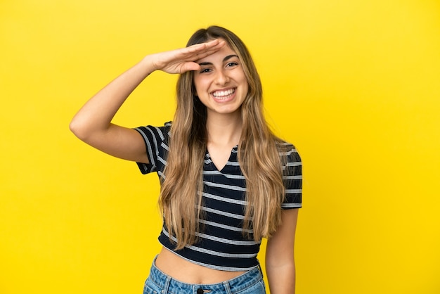 Young caucasian woman isolated on yellow background saluting with hand with happy expression