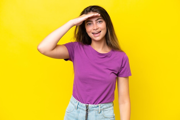 Young caucasian woman isolated on yellow background saluting with hand with happy expression