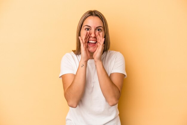 Young caucasian woman isolated on yellow background saying a gossip, pointing to side reporting something.