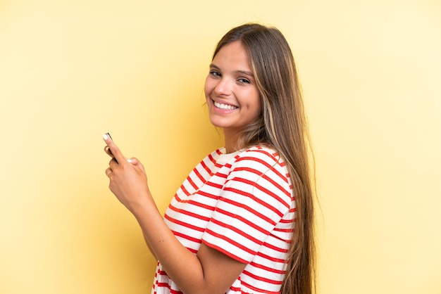 Young caucasian woman isolated on yellow background sending a message or email with the mobile