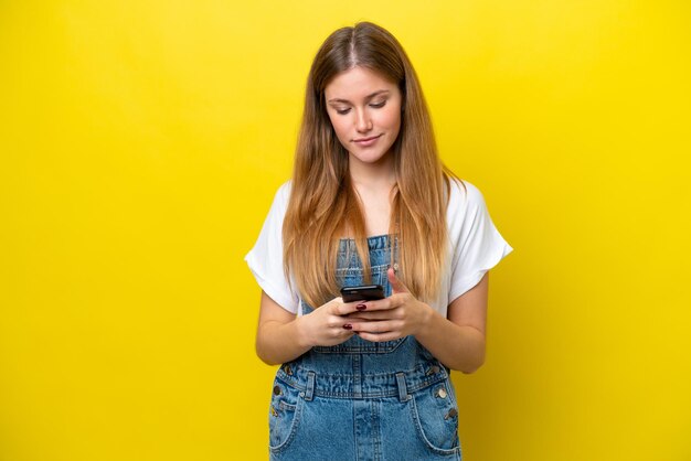 Young caucasian woman isolated on yellow background sending a message with the mobile