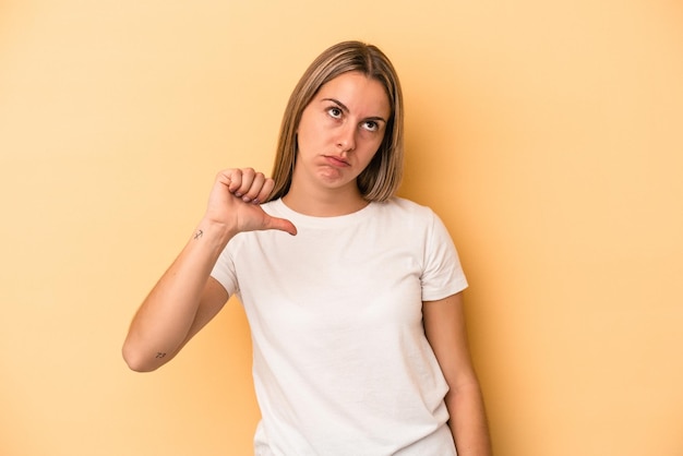 Young caucasian woman isolated on yellow background showing a dislike gesture, thumbs down. Disagreement concept.