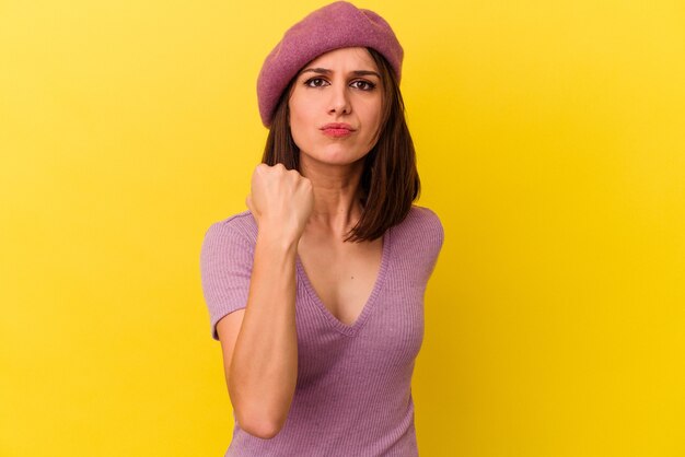 Young caucasian woman isolated on yellow background showing fist to camera, aggressive facial expression.