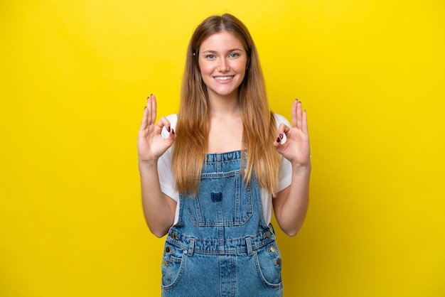 Young caucasian woman isolated on yellow background showing ok sign with two hands