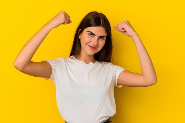 Young caucasian woman isolated on yellow background showing strength gesture with arms, symbol of feminine power