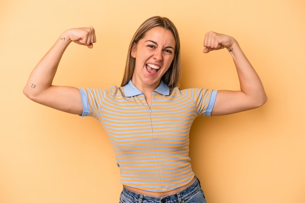 女性の力の象徴である腕で強さのジェスチャーを示す黄色の背景に分離された若い白人女性