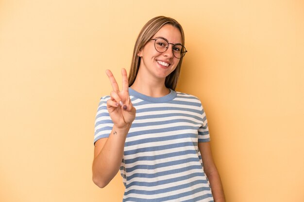 Young caucasian woman isolated on yellow background showing victory sign and smiling broadly.