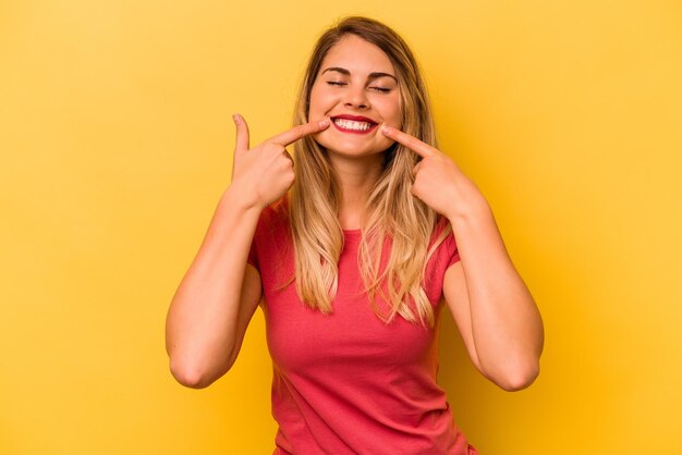 Young caucasian woman isolated on yellow background smiles pointing fingers at mouth