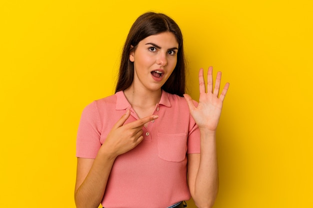 Young caucasian woman isolated on yellow background smiling cheerful showing number five with fingers