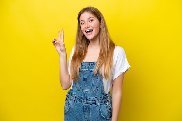 Giovane donna caucasica isolata su sfondo giallo sorridendo e mostrando il segno di vittoria