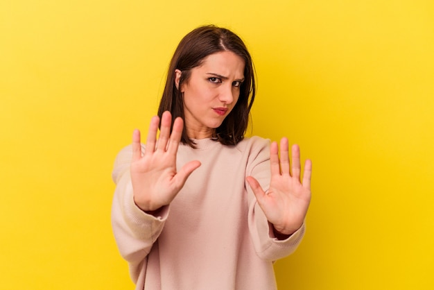 Young caucasian woman isolated on yellow background standing with outstretched hand showing stop sign, preventing you.