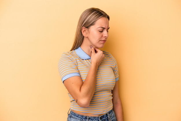 黄色の背景に分離された若い白人女性は、ウイルスや感染症のために喉の痛みに苦しんでいます。