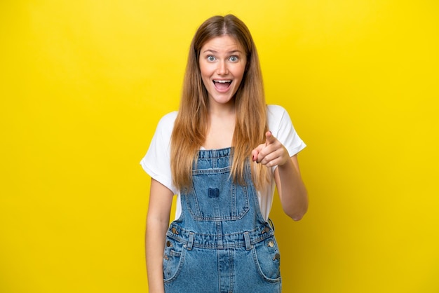 Young caucasian woman isolated on yellow background surprised and pointing front