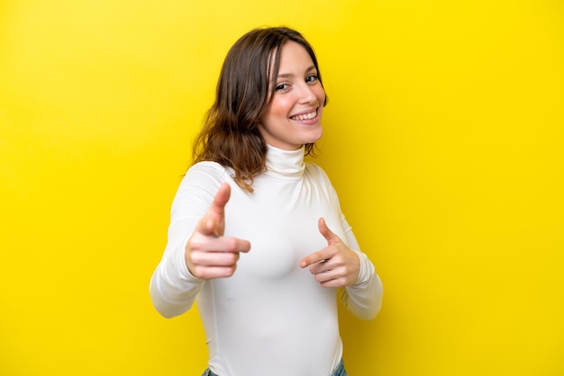 Young caucasian woman isolated on yellow background surprised and pointing front