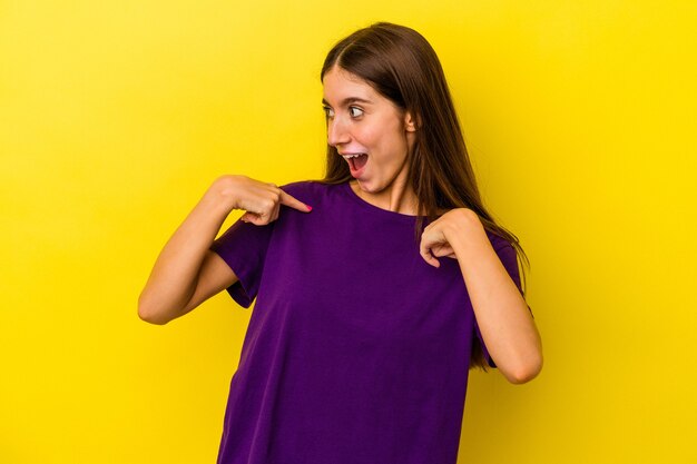 Young caucasian woman isolated on yellow background surprised pointing with finger, smiling broadly.