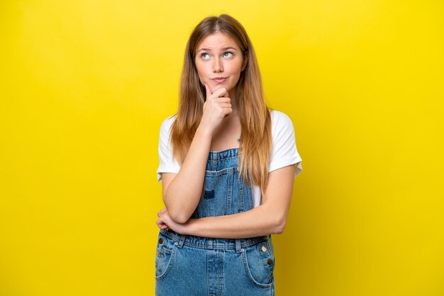 見上げながらアイデアを考えて黄色の背景に分離された若い白人女性