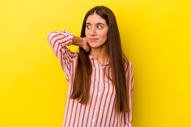 Young caucasian woman isolated on yellow background touching back of head, thinking and making a choice