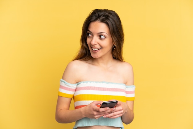 携帯電話を使用して見上げる黄色の背景に分離された若い白人女性