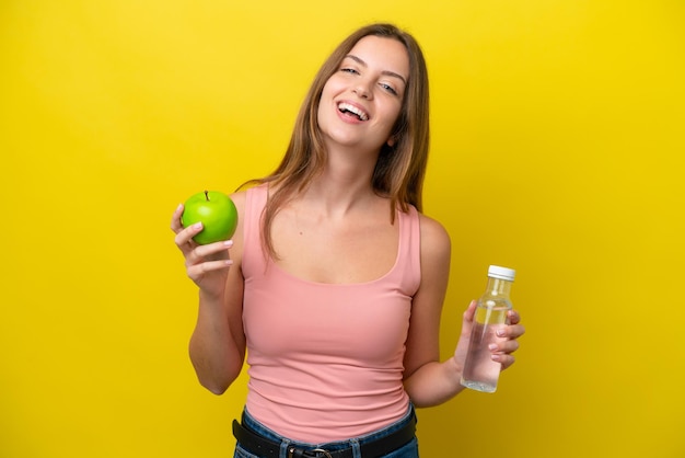 Young caucasian woman isolated on yellow background with an apple and with a bottle of water