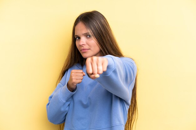 戦闘ジェスチャーで黄色の背景に分離された若い白人女性