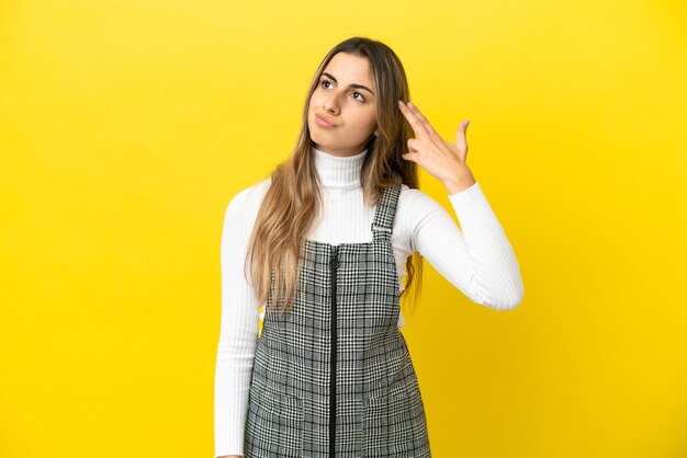 Young caucasian woman isolated on yellow background with problems making suicide gesture