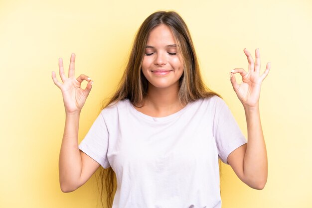 Young caucasian woman isolated on yellow background in zen pose