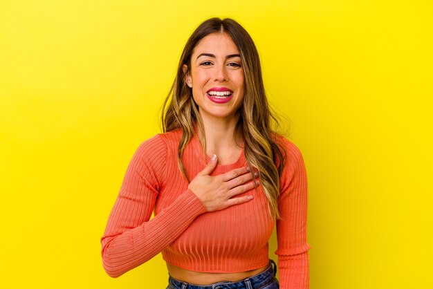 Young caucasian woman isolated on yellow laughs out loudly keeping hand on chest