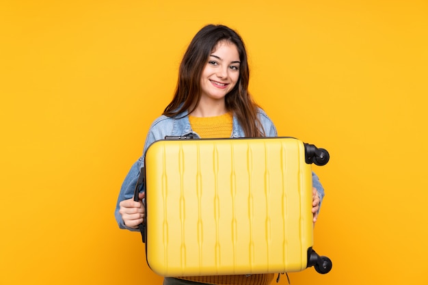 Young caucasian woman isolated on yellow in vacation with travel suitcase