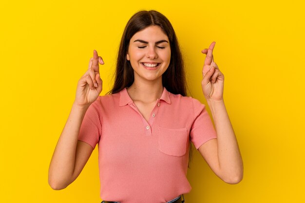 Young caucasian woman isolated on yellow wall crossing fingers for having luck