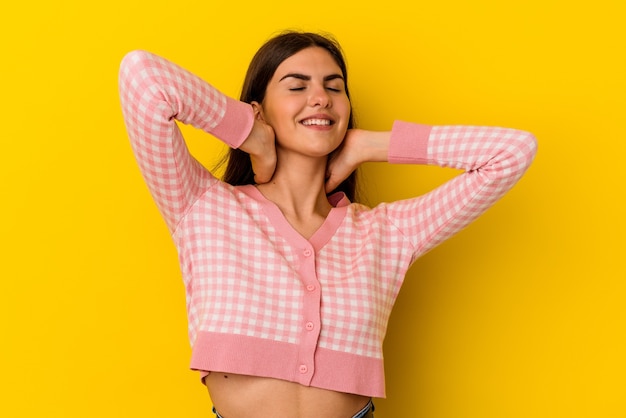 Young caucasian woman isolated on yellow wall feeling confident, with hands behind the head