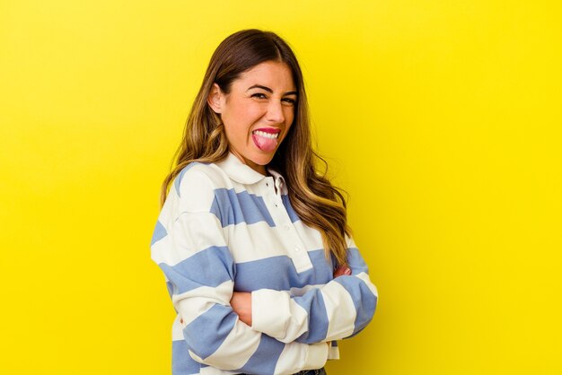 Young caucasian woman isolated on yellow wall funny and friendly sticking out tongue