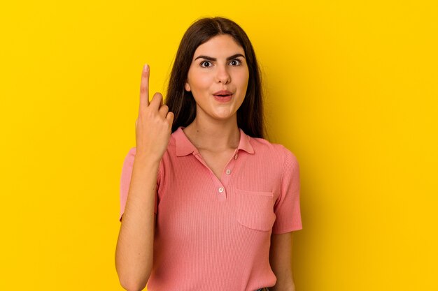 Young caucasian woman isolated on yellow wall pointing upside with opened mouth.