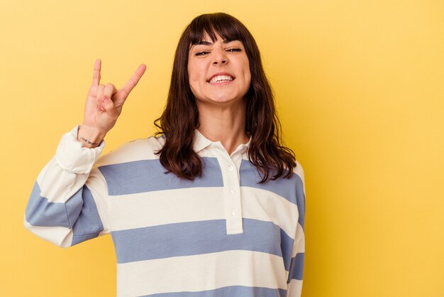 Young caucasian woman isolated on yellow wall showing rock gesture with fingers