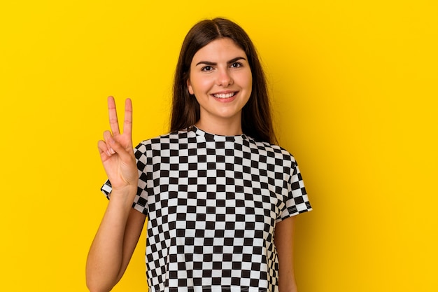 Young caucasian woman isolated on yellow wall showing victory sign and smiling broadly